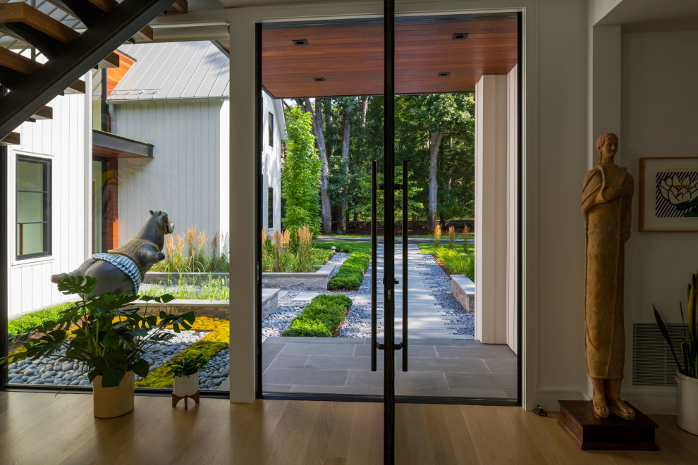 Diseño de entrada moderna con paredes blancas, suelo de madera en tonos medios, puerta doble, puerta negra y suelo beige