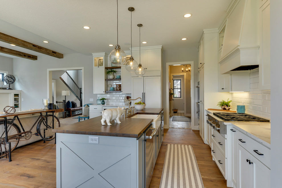 Inspiration for a large country galley open plan kitchen in Minneapolis with a farmhouse sink, wood benchtops, white splashback, subway tile splashback, medium hardwood floors, with island, brown floor, shaker cabinets, white cabinets and panelled appliances.