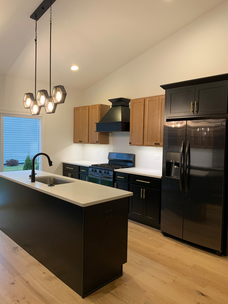 Design ideas for a mid-sized modern galley open plan kitchen in Chicago with an undermount sink, shaker cabinets, black cabinets, quartz benchtops, white splashback, black appliances, vinyl floors, with island, brown floor, white benchtop and vaulted.