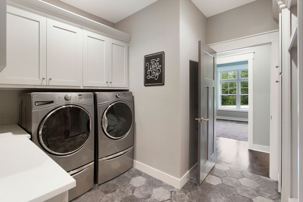Large country l-shaped dedicated laundry room in Kansas City with shaker cabinets, white cabinets, solid surface benchtops, grey walls, porcelain floors, a side-by-side washer and dryer, grey floor and white benchtop.