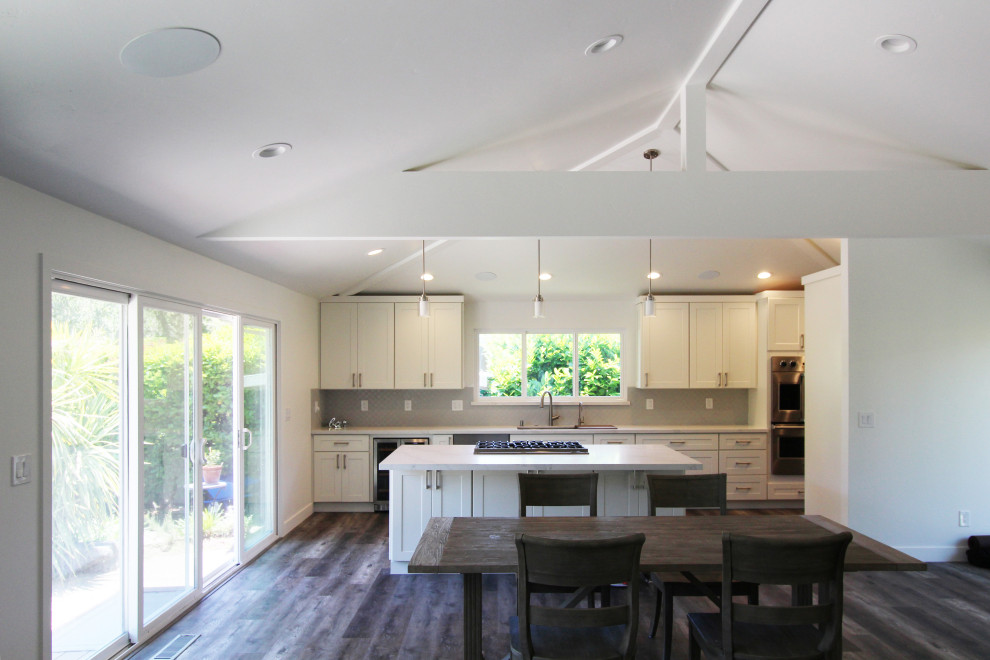 Open concept kitchen - large transitional single-wall vinyl floor and brown floor open concept kitchen idea with an undermount sink, shaker cabinets, white cabinets, quartz countertops, gray backsplash, ceramic backsplash, stainless steel appliances, an island and white countertops