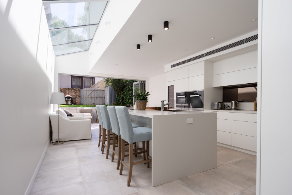 This is an example of a contemporary l-shaped kitchen in Sydney with flat-panel cabinets, white cabinets, stainless steel appliances, with island, grey floor and grey benchtop.