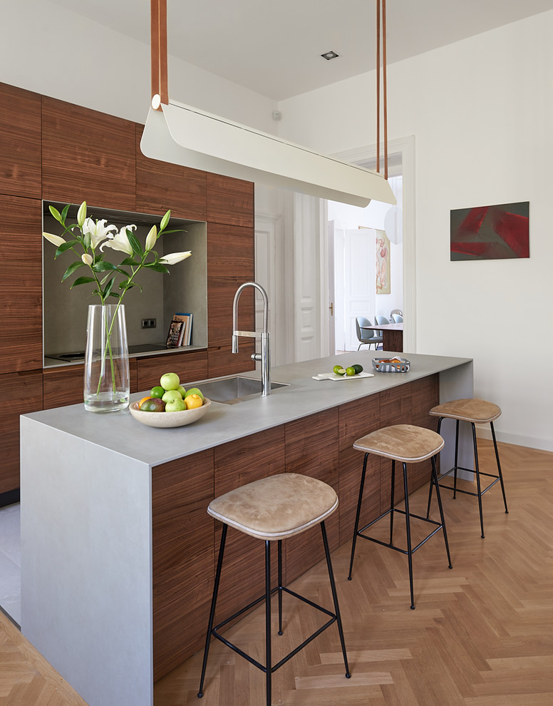 Photo of a large contemporary kitchen in Other with medium wood cabinets, concrete benchtops, grey splashback, cement tile splashback, with island, a single-bowl sink, flat-panel cabinets and light hardwood floors.