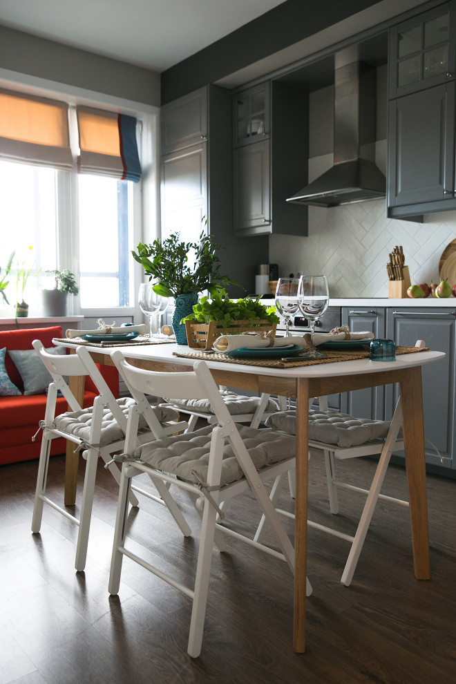 Small scandinavian single-wall eat-in kitchen in Saint Petersburg with a single-bowl sink, raised-panel cabinets, grey cabinets, solid surface benchtops, white splashback, ceramic splashback, stainless steel appliances, laminate floors, no island, brown floor and white benchtop.