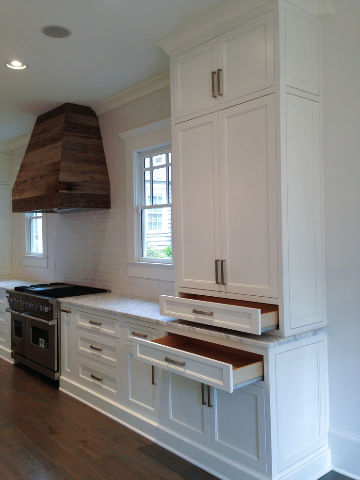 Photo of a mid-sized arts and crafts l-shaped eat-in kitchen in Atlanta with an undermount sink, shaker cabinets, white cabinets, marble benchtops, white splashback, ceramic splashback, stainless steel appliances, light hardwood floors, with island, grey floor and white benchtop.
