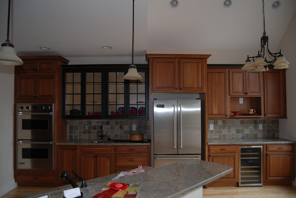 This is an example of a mid-sized transitional u-shaped kitchen in Raleigh with an undermount sink, raised-panel cabinets, medium wood cabinets, granite benchtops, brown splashback, stone tile splashback, stainless steel appliances, light hardwood floors, with island and blue floor.