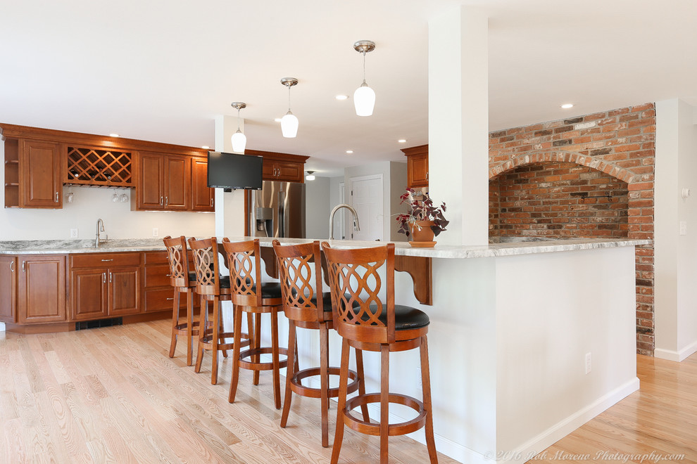 Large eclectic l-shaped open plan kitchen in Manchester with an undermount sink, raised-panel cabinets, medium wood cabinets, granite benchtops, stainless steel appliances, light hardwood floors, with island and beige floor.