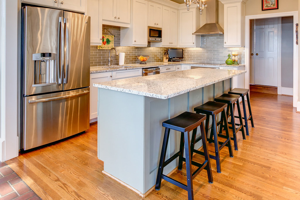 Example of a mid-sized l-shaped light wood floor open concept kitchen design in Birmingham with a single-bowl sink, flat-panel cabinets, white cabinets, granite countertops, gray backsplash, glass tile backsplash, stainless steel appliances and an island