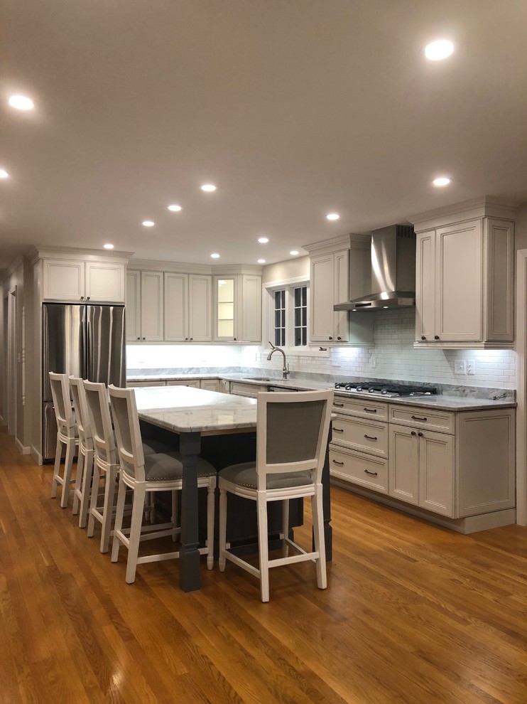 Photo of a mid-sized traditional l-shaped open plan kitchen in Boston with an undermount sink, recessed-panel cabinets, white cabinets, quartzite benchtops, white splashback, subway tile splashback, stainless steel appliances, medium hardwood floors, with island, brown floor and grey benchtop.