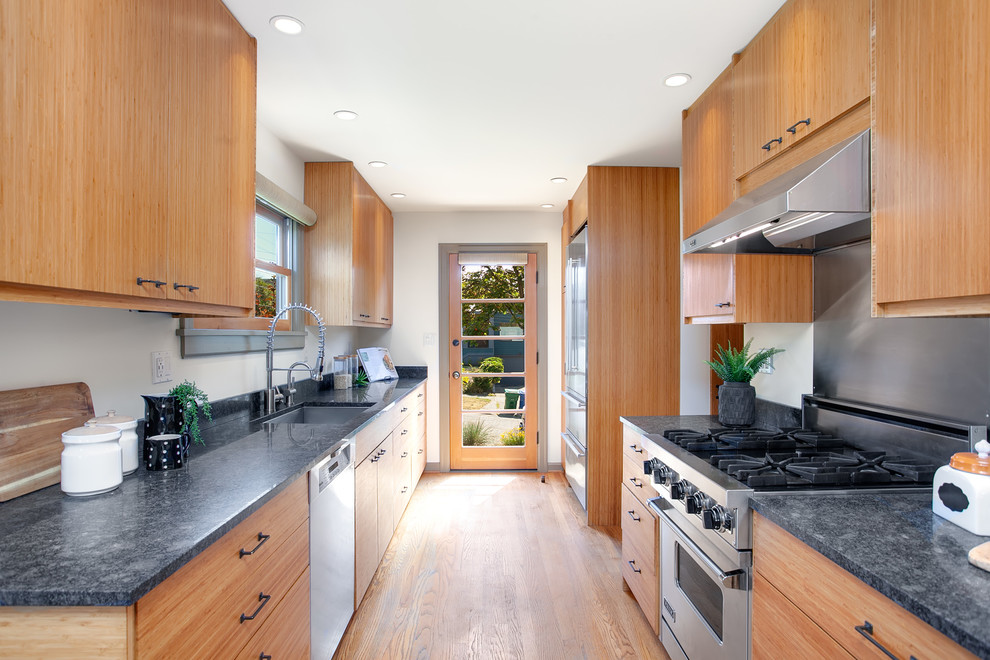 Enclosed kitchen - small transitional galley medium tone wood floor and brown floor enclosed kitchen idea in Seattle with a farmhouse sink, flat-panel cabinets, medium tone wood cabinets, granite countertops, stainless steel appliances, no island and gray countertops