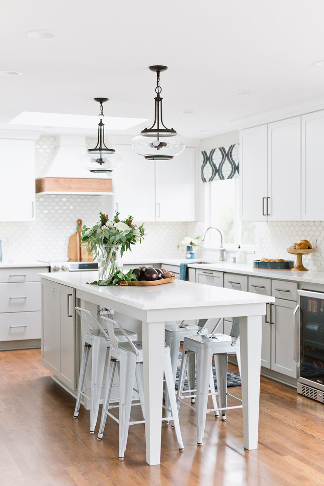 Open concept kitchen - mid-sized transitional l-shaped medium tone wood floor and brown floor open concept kitchen idea with an undermount sink, shaker cabinets, white cabinets, quartz countertops, white backsplash, porcelain backsplash, stainless steel appliances, an island and white countertops