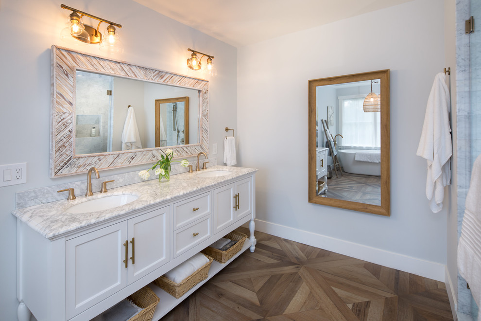 This is an example of a large country master bathroom in San Francisco with flat-panel cabinets, white cabinets, a freestanding tub, a corner shower, a one-piece toilet, white tile, marble, white walls, porcelain floors, an integrated sink, marble benchtops, brown floor and a hinged shower door.