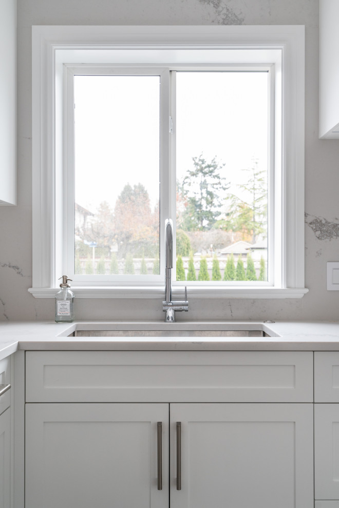 Inspiration for an expansive traditional galley eat-in kitchen in Vancouver with an undermount sink, shaker cabinets, white cabinets, quartz benchtops, white splashback, stone slab splashback, stainless steel appliances, medium hardwood floors, a peninsula, grey floor and white benchtop.