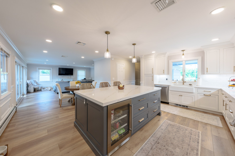 Inspiration for a mid-sized modern l-shaped open plan kitchen in Newark with beaded inset cabinets, white cabinets, marble benchtops, white splashback, brick splashback, stainless steel appliances, vinyl floors, with island, beige floor, white benchtop and a farmhouse sink.