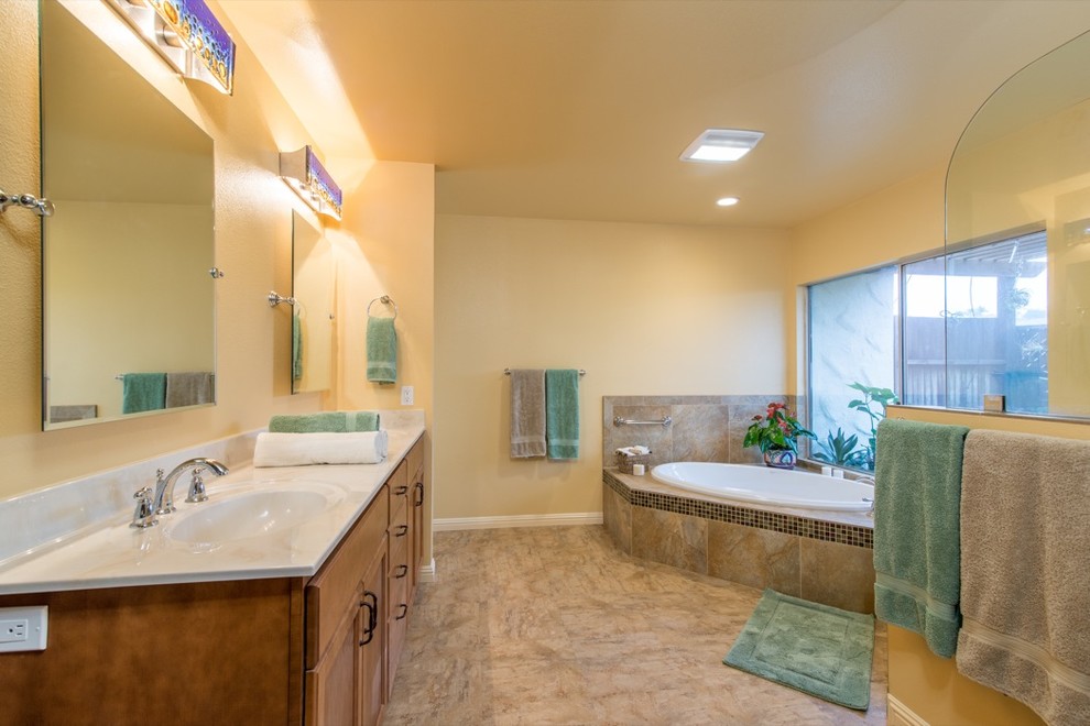 Large tropical master bathroom in San Diego with flat-panel cabinets, light wood cabinets, a drop-in tub, an alcove shower, brown tile, glass tile, yellow walls, linoleum floors, an integrated sink and marble benchtops.