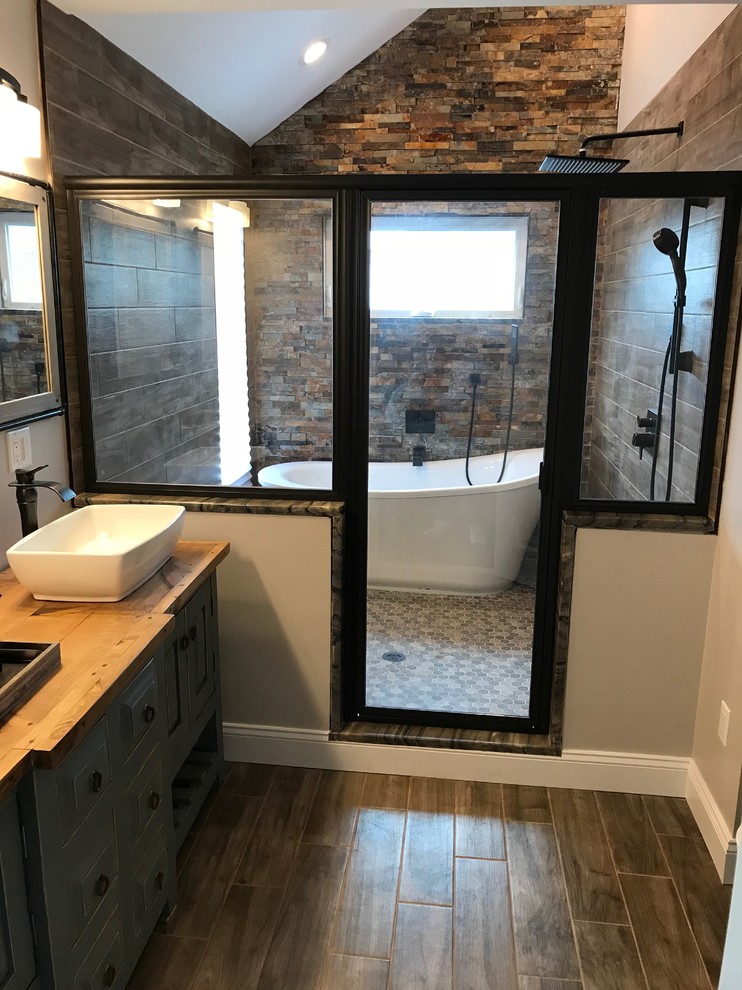 Design ideas for a mid-sized transitional master wet room bathroom in Newark with a freestanding tub, a two-piece toilet, beige tile, stone tile, beige walls, ceramic floors, a vessel sink, wood benchtops, beige floor and a hinged shower door.