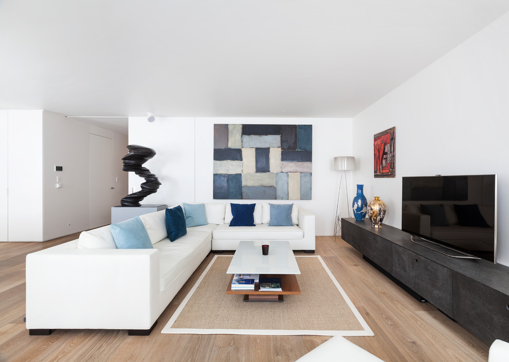 This is an example of a large contemporary formal open concept living room in London with white walls, a freestanding tv, light hardwood floors and beige floor.