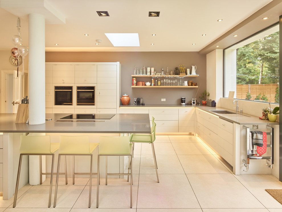 This is an example of a large modern l-shaped kitchen in West Midlands with an undermount sink, flat-panel cabinets, white cabinets, with island, white floor, grey benchtop and stainless steel appliances.