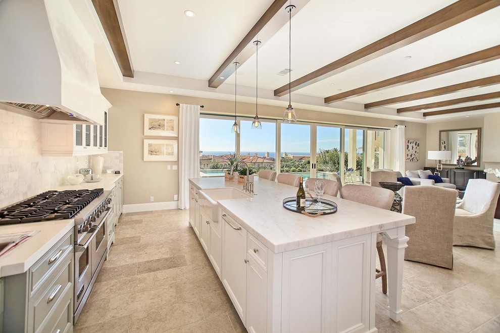 Inspiration for a large mediterranean galley open plan kitchen in Orange County with a farmhouse sink, glass-front cabinets, white cabinets, marble benchtops, stainless steel appliances, limestone floors, with island and beige floor.