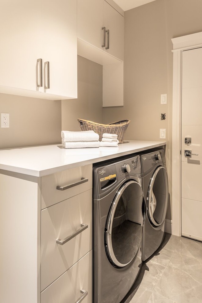 Design ideas for a mid-sized contemporary single-wall dedicated laundry room in Vancouver with flat-panel cabinets, white cabinets, solid surface benchtops, beige walls, concrete floors, a side-by-side washer and dryer, grey floor and white benchtop.
