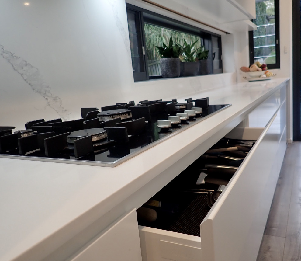 Design ideas for a large contemporary galley eat-in kitchen in Sydney with an undermount sink, flat-panel cabinets, white cabinets, quartz benchtops, white splashback, stone slab splashback, black appliances, medium hardwood floors, with island and white benchtop.