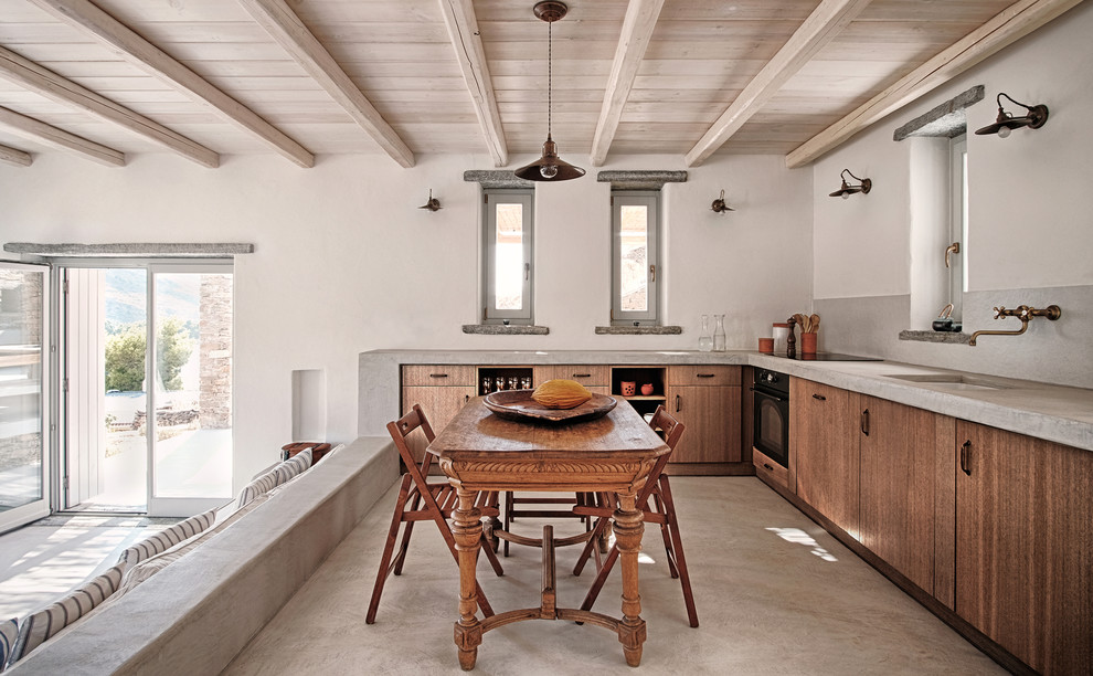 Inspiration for a mid-sized mediterranean l-shaped eat-in kitchen in Barcelona with an undermount sink, flat-panel cabinets, medium wood cabinets, limestone benchtops, grey splashback, black appliances, no island, concrete floors, grey floor and grey benchtop.