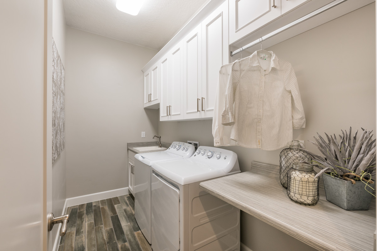 Transitional single-wall dedicated laundry room in Salt Lake City with a drop-in sink, recessed-panel cabinets, white cabinets, solid surface benchtops, a side-by-side washer and dryer and grey walls.