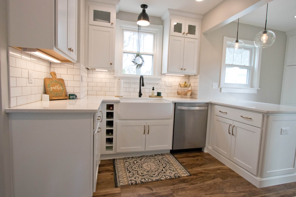 Mid-sized mountain style galley vinyl floor and brown floor enclosed kitchen photo with a farmhouse sink, recessed-panel cabinets, white cabinets, quartz countertops, white backsplash, subway tile backsplash, stainless steel appliances, a peninsula and white countertops