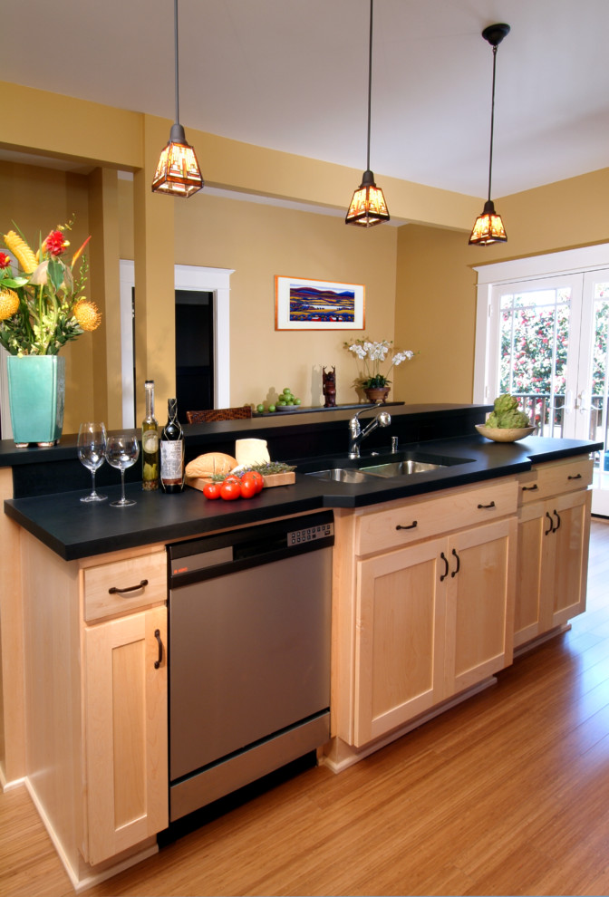 This is an example of a transitional l-shaped eat-in kitchen in Portland with an undermount sink, shaker cabinets, light wood cabinets, black splashback and stainless steel appliances.
