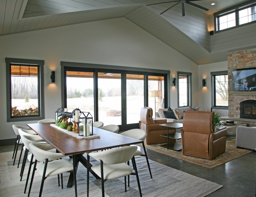 Photo of a mid-sized country open plan dining in Milwaukee with grey walls, concrete floors, a wood stove, a stone fireplace surround, grey floor, vaulted and wood walls.