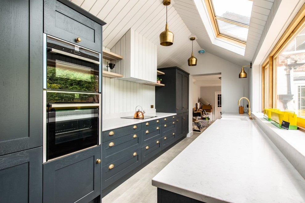 Photo of a mid-sized transitional galley separate kitchen in Kent with shaker cabinets, blue cabinets, no island, grey floor, a farmhouse sink, panelled appliances and grey benchtop.