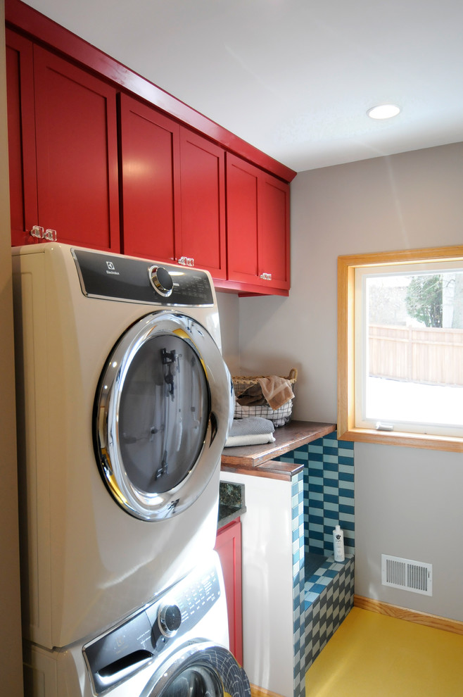 Photo of a mid-sized contemporary single-wall utility room in Minneapolis with an undermount sink, shaker cabinets, red cabinets, wood benchtops, beige walls, laminate floors, a stacked washer and dryer and yellow floor.