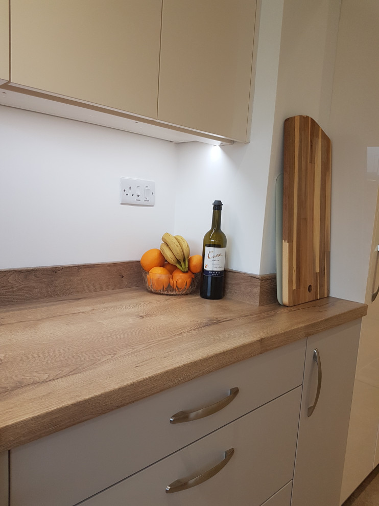 This is an example of a small contemporary u-shaped separate kitchen in West Midlands with a double-bowl sink, flat-panel cabinets, beige cabinets, laminate benchtops, orange splashback, glass sheet splashback, black appliances, vinyl floors, no island, brown floor and brown benchtop.