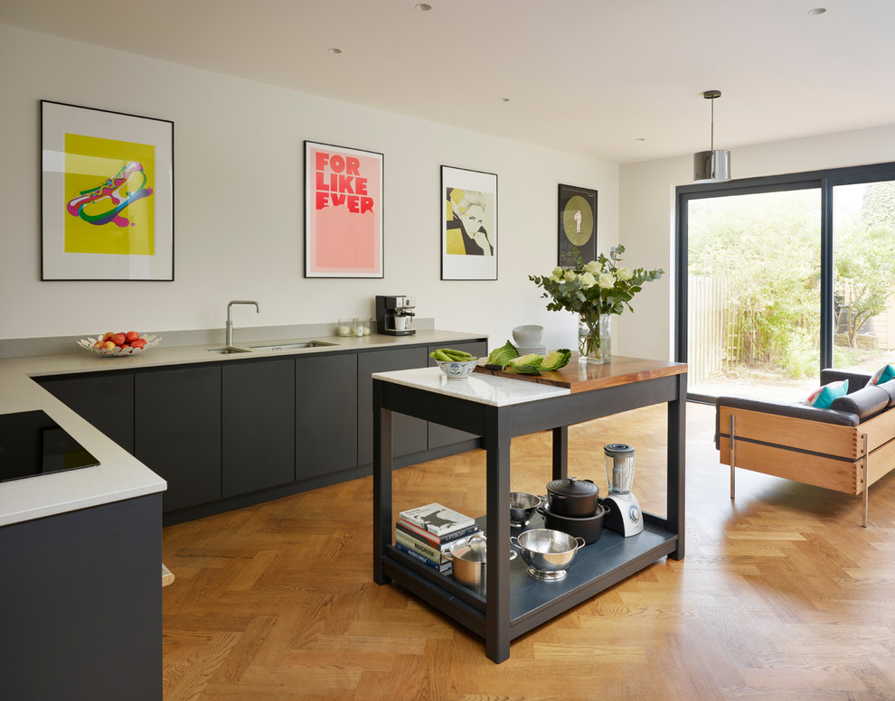 Inspiration for a large scandinavian l-shaped open plan kitchen in London with flat-panel cabinets, solid surface benchtops, medium hardwood floors, with island, white benchtop, a double-bowl sink and black cabinets.