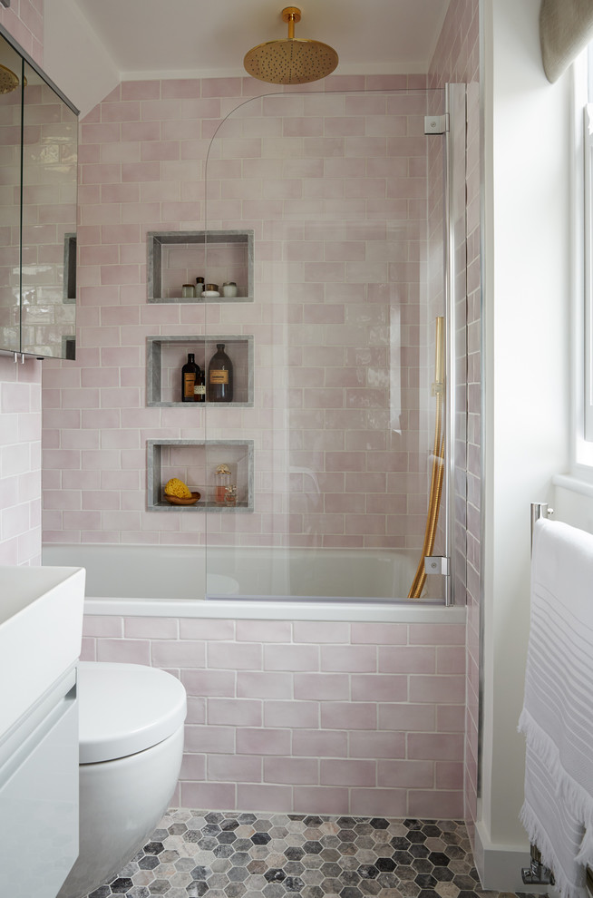 Design ideas for a small transitional bathroom in London with flat-panel cabinets, a drop-in tub, a shower/bathtub combo, pink tile, white walls, ceramic floors, grey cabinets, subway tile, multi-coloured floor and white benchtops.