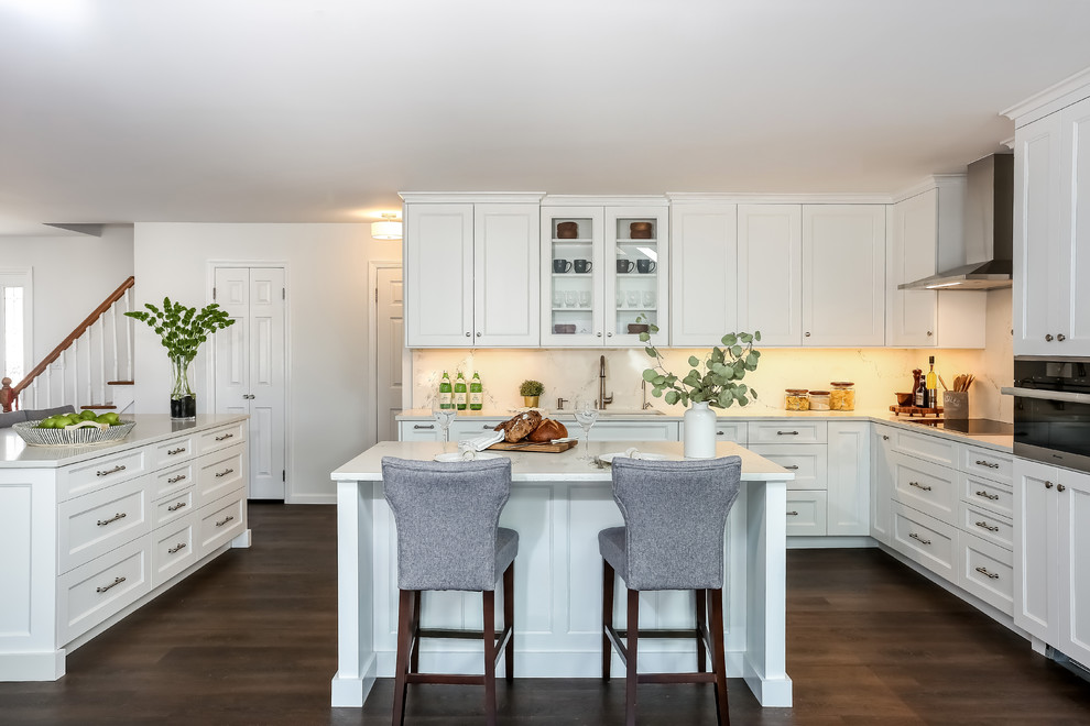 Photo of a mid-sized traditional l-shaped kitchen in New York with an undermount sink, white cabinets, quartz benchtops, white splashback, stone slab splashback, stainless steel appliances, dark hardwood floors, multiple islands, brown floor, shaker cabinets and grey benchtop.