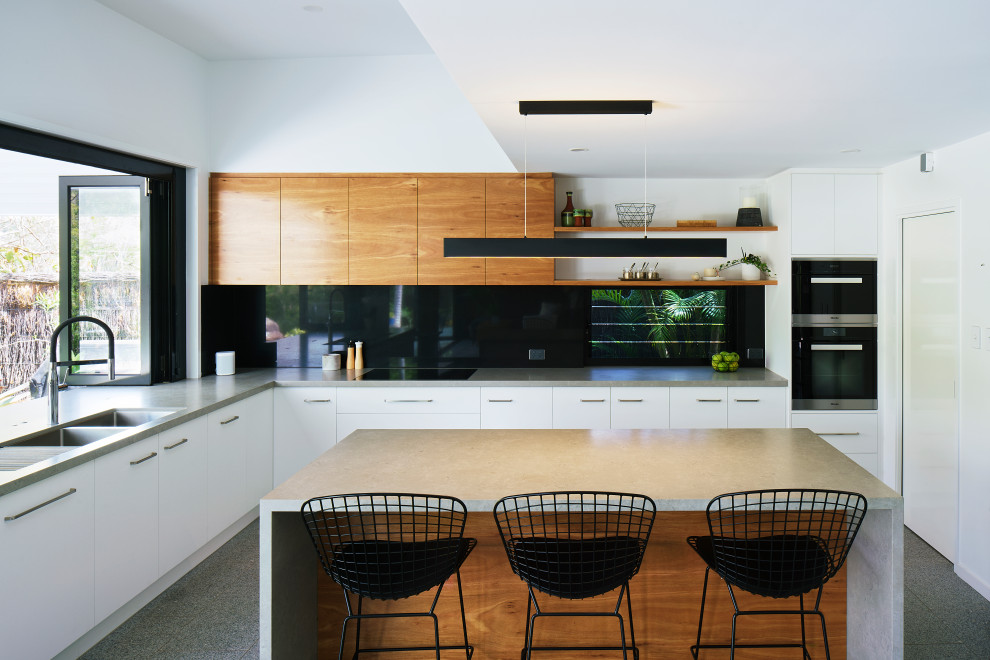 Photo of a mid-sized contemporary l-shaped open plan kitchen in Brisbane with an undermount sink, flat-panel cabinets, light wood cabinets, quartz benchtops, black splashback, stone slab splashback, black appliances, ceramic floors, with island, grey floor and grey benchtop.