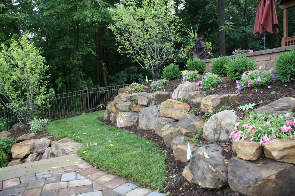 Photo of an expansive traditional sloped full sun garden in Indianapolis with a retaining wall and concrete pavers.