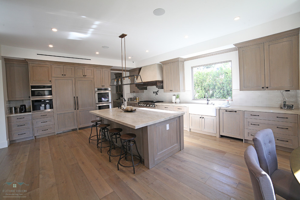 Photo of an expansive midcentury kitchen in Los Angeles with distressed cabinets, marble benchtops, white splashback, porcelain splashback, stainless steel appliances, medium hardwood floors, with island and brown floor.