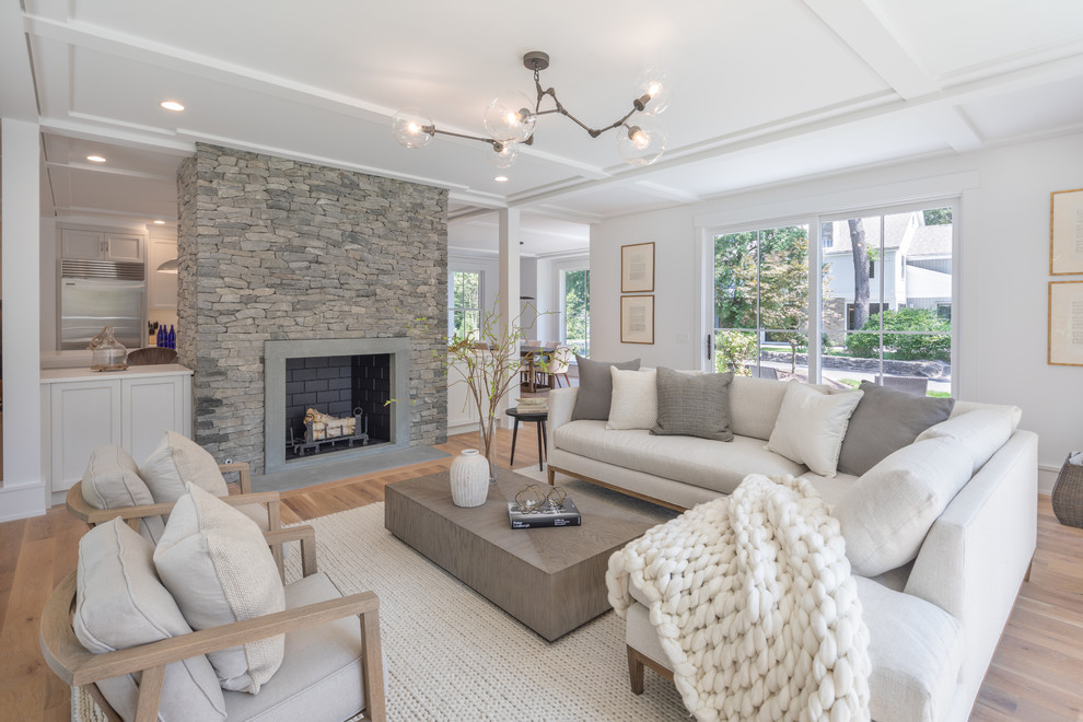 This is an example of a large country open concept living room in New York with white walls, a standard fireplace, a stone fireplace surround, medium hardwood floors and brown floor.