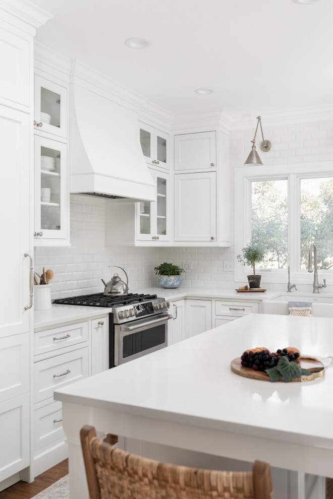 Example of a mid-sized transitional l-shaped medium tone wood floor and brown floor eat-in kitchen design in Chicago with a farmhouse sink, beaded inset cabinets, white cabinets, quartz countertops, white backsplash, ceramic backsplash, paneled appliances, an island and white countertops