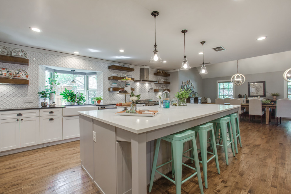 Inspiration for a large arts and crafts single-wall open plan kitchen in Dallas with a farmhouse sink, shaker cabinets, white cabinets, quartz benchtops, white splashback, ceramic splashback, stainless steel appliances, medium hardwood floors and with island.