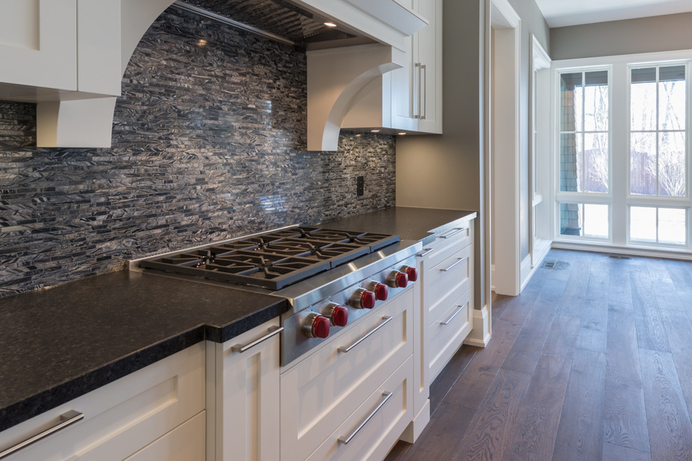 This is an example of a large transitional l-shaped separate kitchen in Toronto with a single-bowl sink, shaker cabinets, white cabinets, granite benchtops, black splashback, mosaic tile splashback, white appliances, medium hardwood floors and with island.