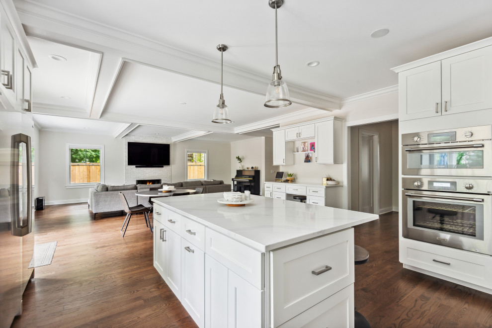 Inspiration for a large contemporary u-shaped eat-in kitchen in Chicago with a farmhouse sink, shaker cabinets, white cabinets, quartzite benchtops, white splashback, porcelain splashback, stainless steel appliances, medium hardwood floors, with island, brown floor, white benchtop and coffered.