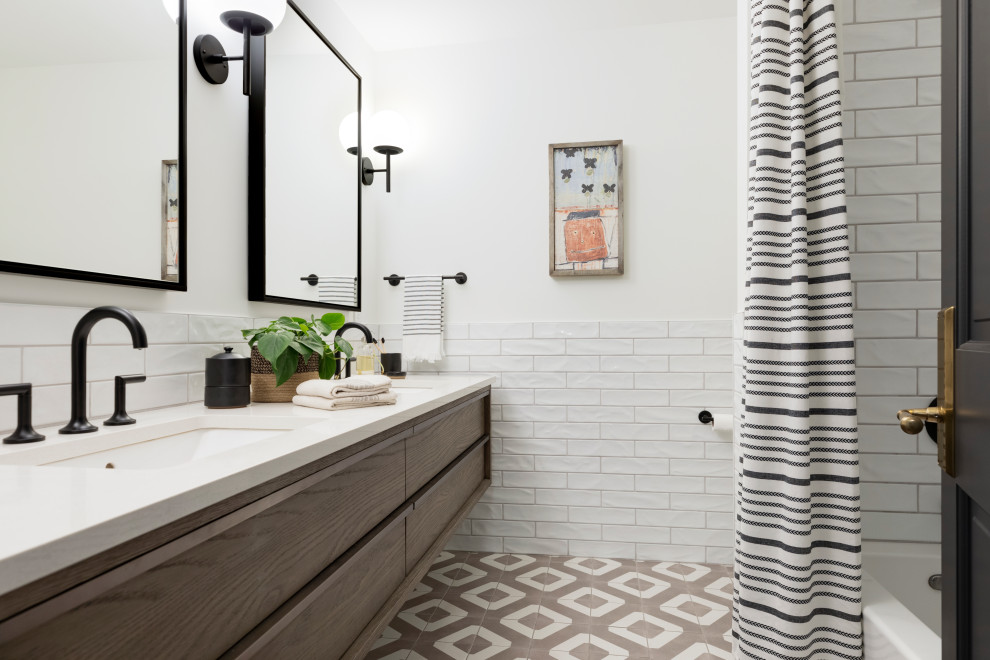 This is an example of a transitional kids bathroom in Minneapolis with flat-panel cabinets, medium wood cabinets, an alcove tub, a shower/bathtub combo, white tile, ceramic tile, porcelain floors, an undermount sink, engineered quartz benchtops, multi-coloured floor, a shower curtain and white benchtops.