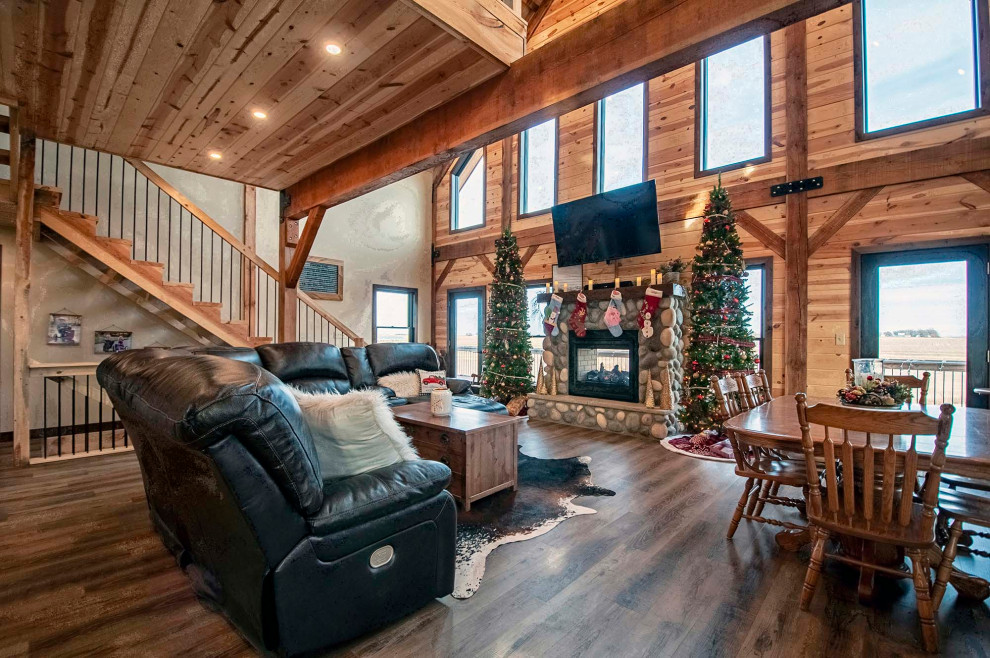 This is an example of a small country open concept family room with beige walls, medium hardwood floors, a standard fireplace, a stone fireplace surround, a wall-mounted tv, brown floor, exposed beam and wood walls.