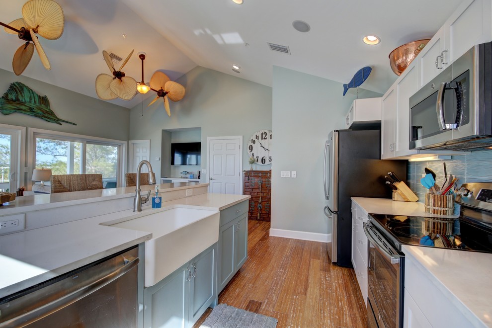 This is an example of a mid-sized beach style single-wall open plan kitchen in Tampa with a farmhouse sink, shaker cabinets, white cabinets, solid surface benchtops, blue splashback, ceramic splashback, stainless steel appliances, bamboo floors, with island and brown floor.