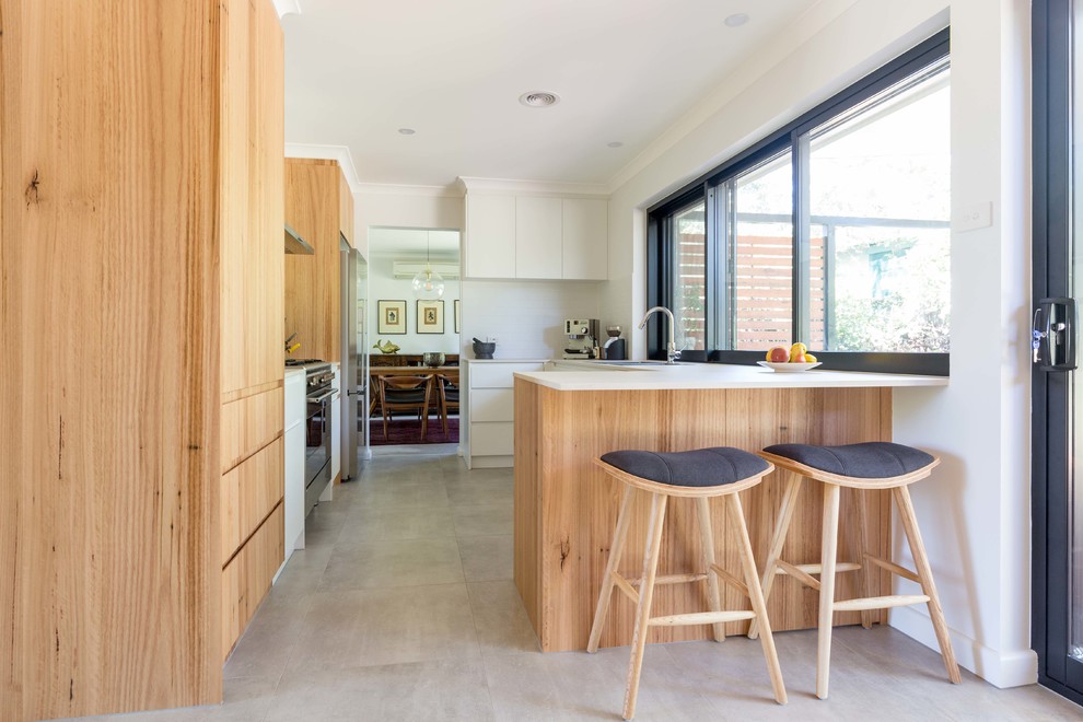 This is an example of a mid-sized contemporary galley separate kitchen in Canberra - Queanbeyan with a double-bowl sink, flat-panel cabinets, light wood cabinets, laminate benchtops, white splashback, porcelain splashback, stainless steel appliances, ceramic floors, a peninsula and grey floor.