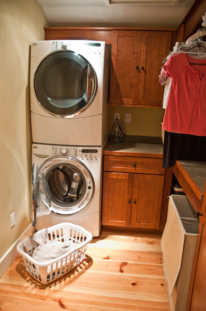 Design ideas for a traditional laundry room in Philadelphia with shaker cabinets, medium wood cabinets, beige walls, light hardwood floors and a stacked washer and dryer.