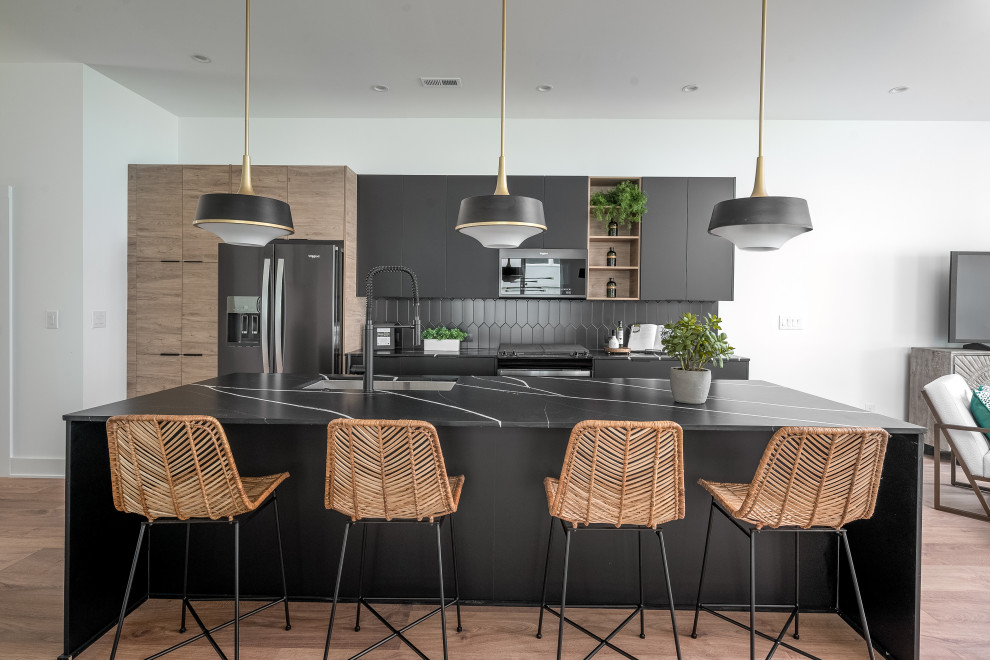 Photo of a contemporary galley open plan kitchen in Charlotte with a submerged sink, flat-panel cabinets, black cabinets, engineered stone countertops, black splashback, ceramic splashback, stainless steel appliances, laminate floors, an island, brown floors and black worktops.